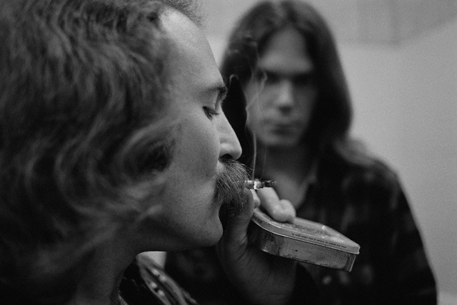 12 Jul 1970, USA --- Musician David Crosby smokes a cigarette while Neil Young looks on. They are in a backstage bathroom. --- Image by © Henry Diltz/CORBIS
